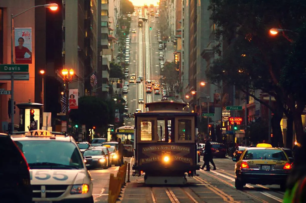 San Francisco street with a cable car, taxis, and uphill traffic at dusk.