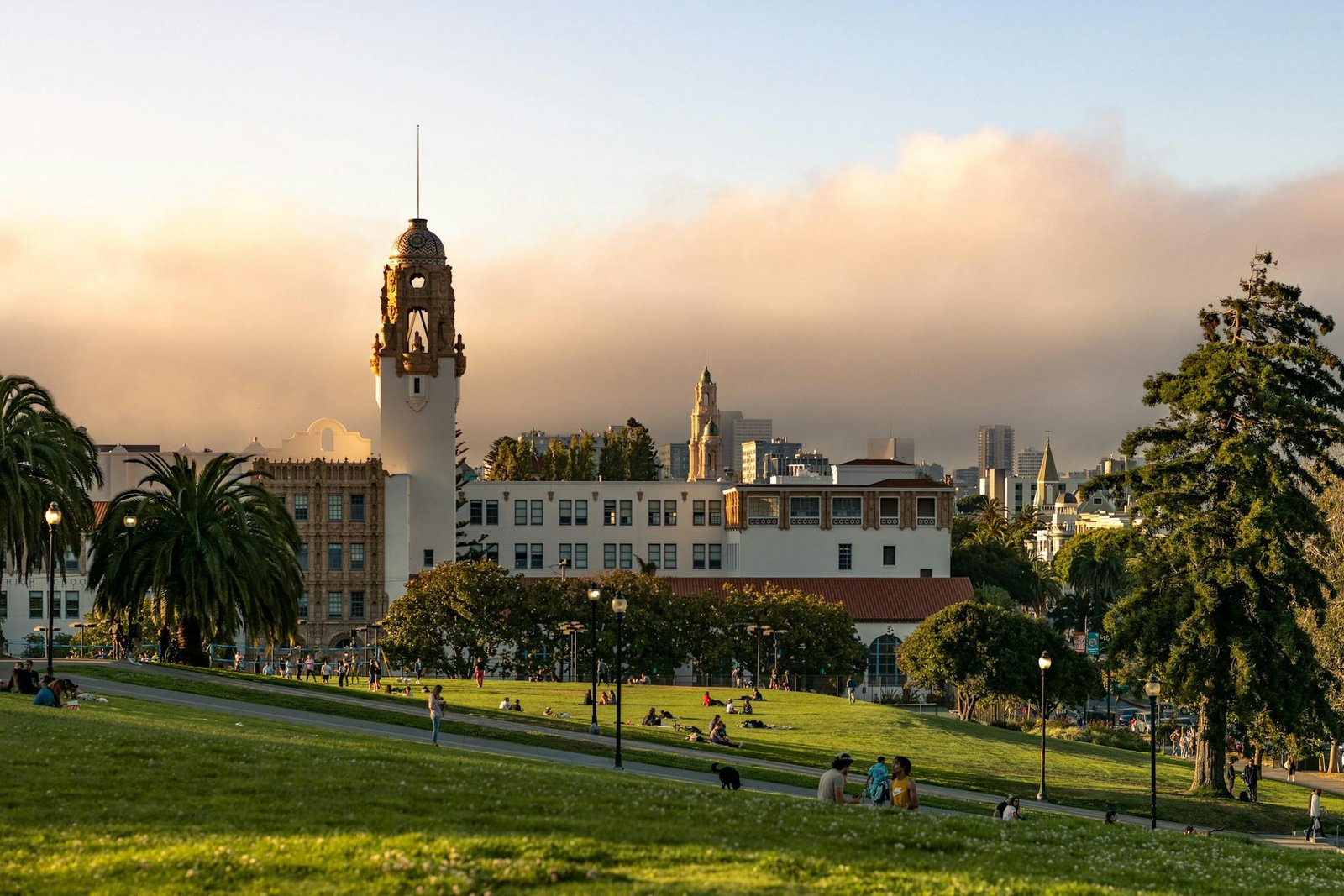 Historic building with a clock tower, park, and city skyline at sunset