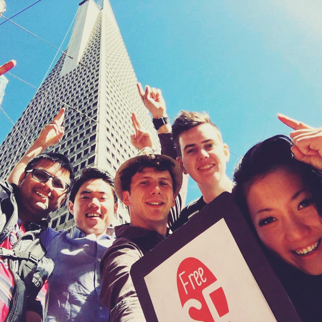 Group of five people posing outdoors with a tall building in the background