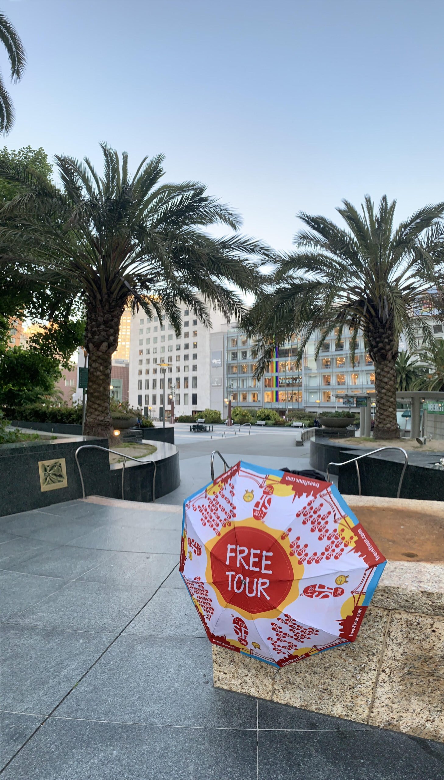 Colorful umbrella with "FREE TOUR" text in a palm-lined plaza