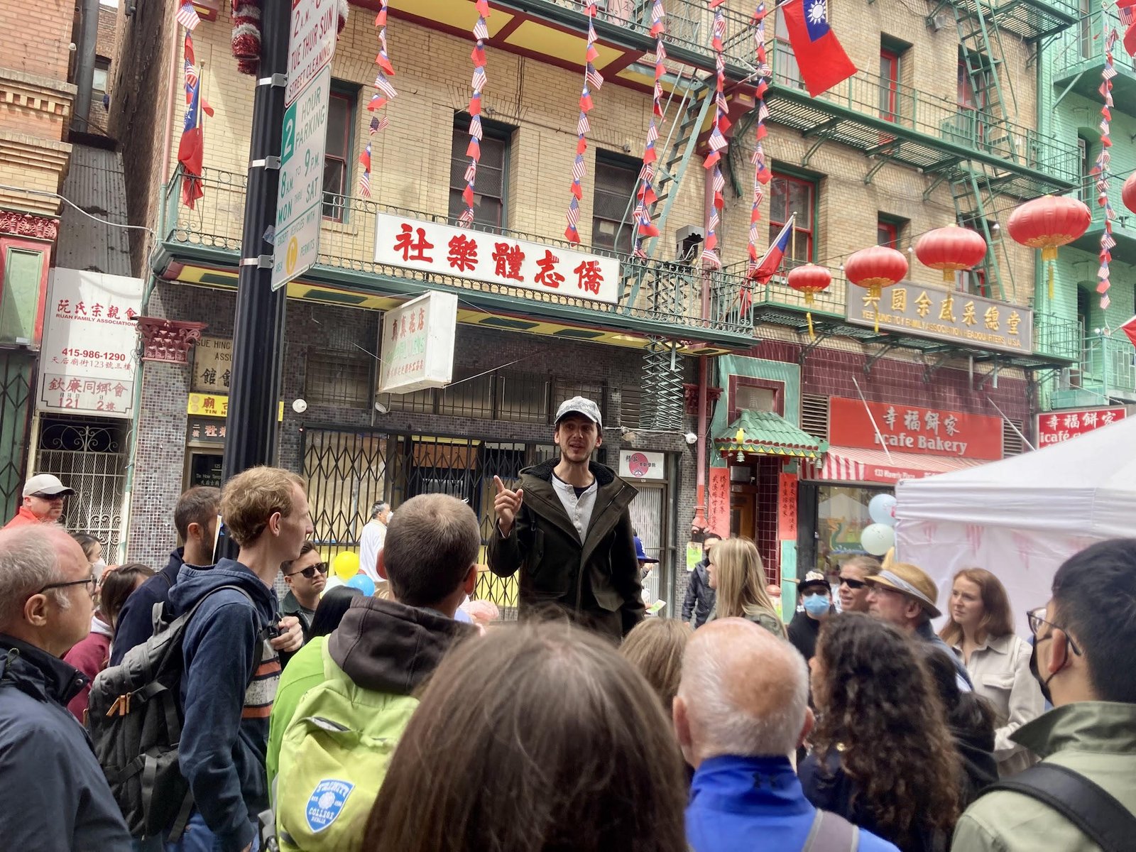 Crowd gathered around a speaker in a vibrant Chinatown setting with lanterns and banners